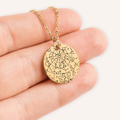 Hand holding a gold coin pendent engraved with a custom star map in a natural color background.