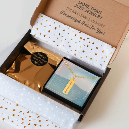 Personalized gold paperclip necklace with a vertical bar pendant engraved with a unique inspiration mantra, packaging in a gift box with a greeting card and gold confetti paper, held by hands against a neutral background.