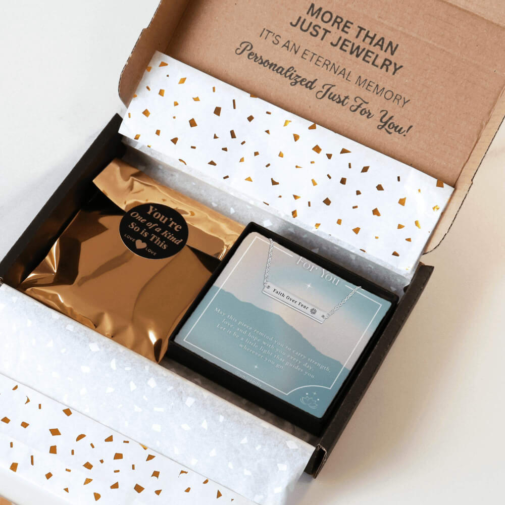 Personalized silver necklace with a bar pendant engraved with a unique inspiration mantra, packaging in a gift box with a greeting card and gold confetti paper, held by hands against a neutral background.