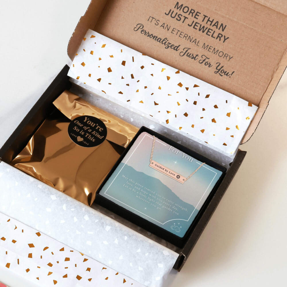 Personalized rose gold necklace with a bar pendant engraved with a unique inspiration mantra, packaging in a gift box with a greeting card and gold confetti paper, held by hands against a neutral background.