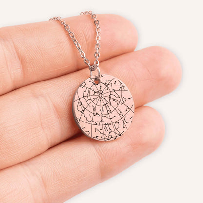 Hand holding a rose gold coin pendent engraved with a custom star map in a natural color background.