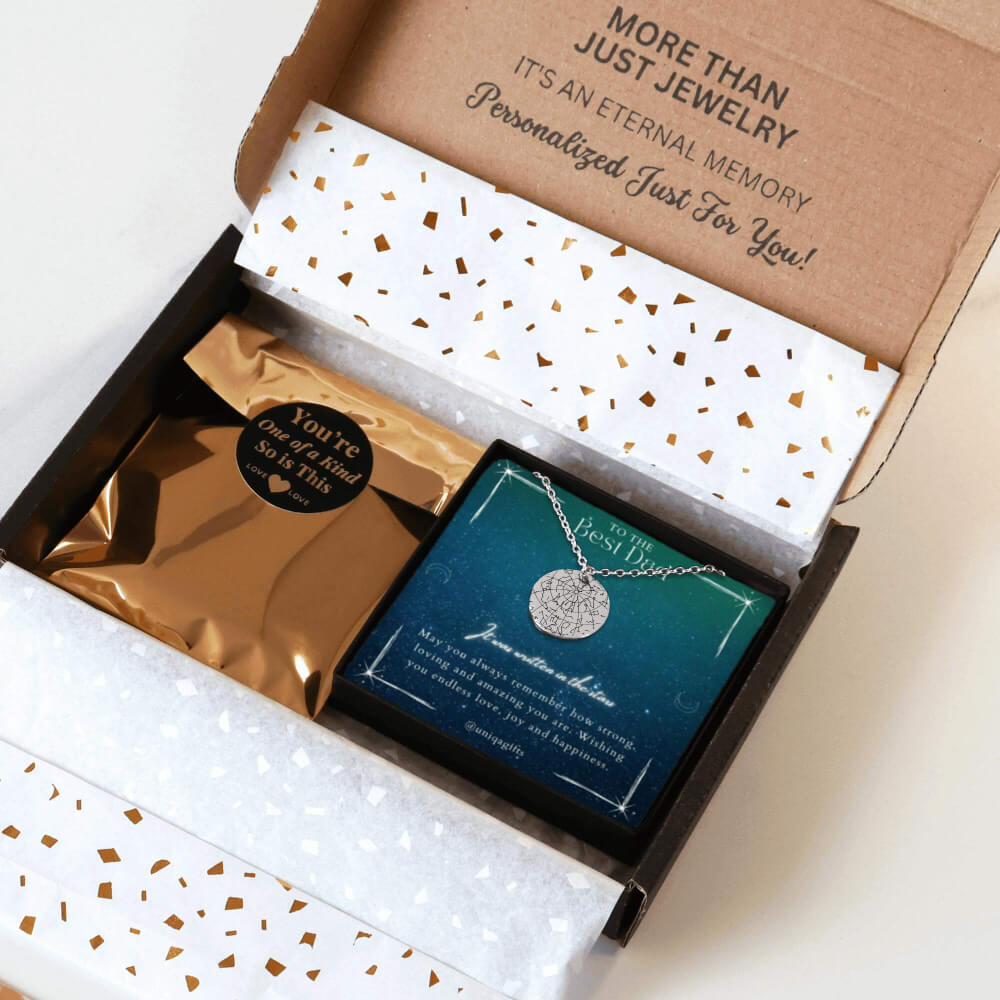 Personalized silver necklace with a coin pendant engraved in custom star map, packaging in a gift box with a festive greeting card for best dad and gold confetti paper, held by hands against a neutral background.