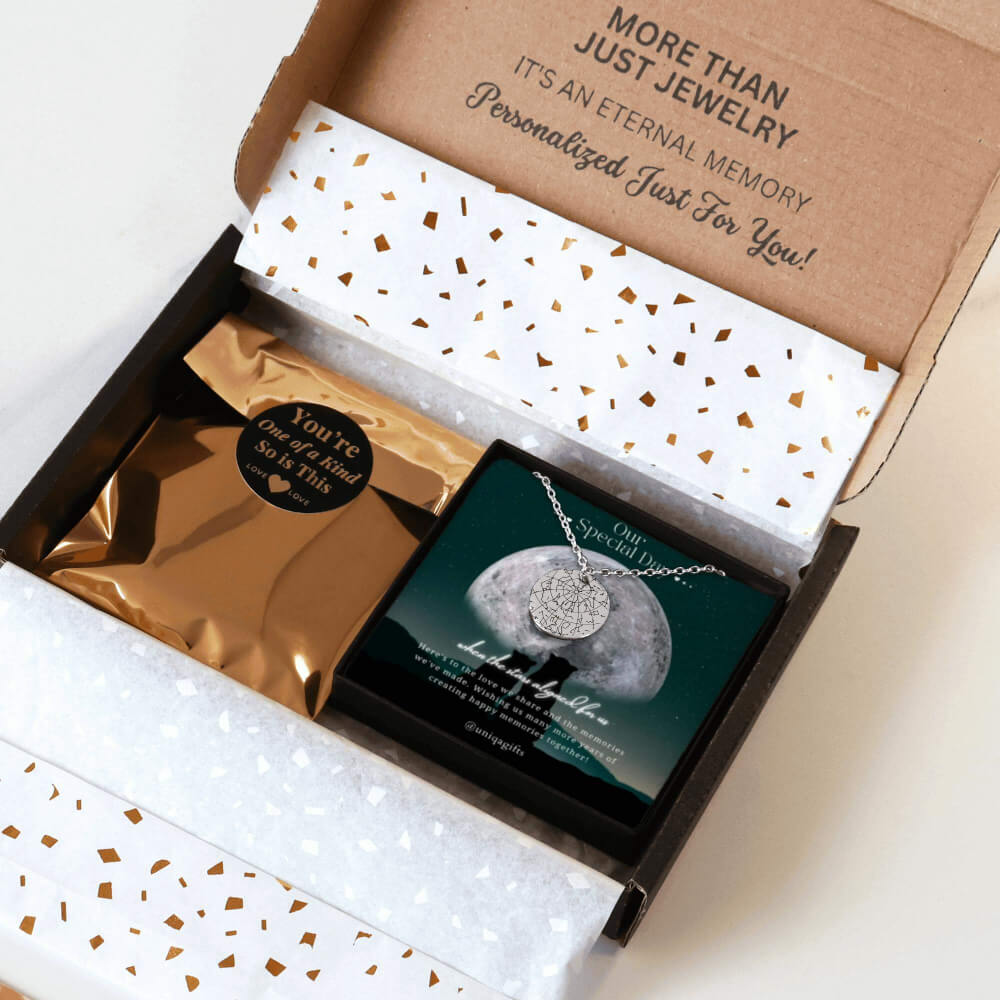 Personalized silver necklace with a coin pendant engraved in custom star map, packaging in a gift box with a festive greeting card for couples anniversary and gold confetti paper, held by hands against a neutral background.