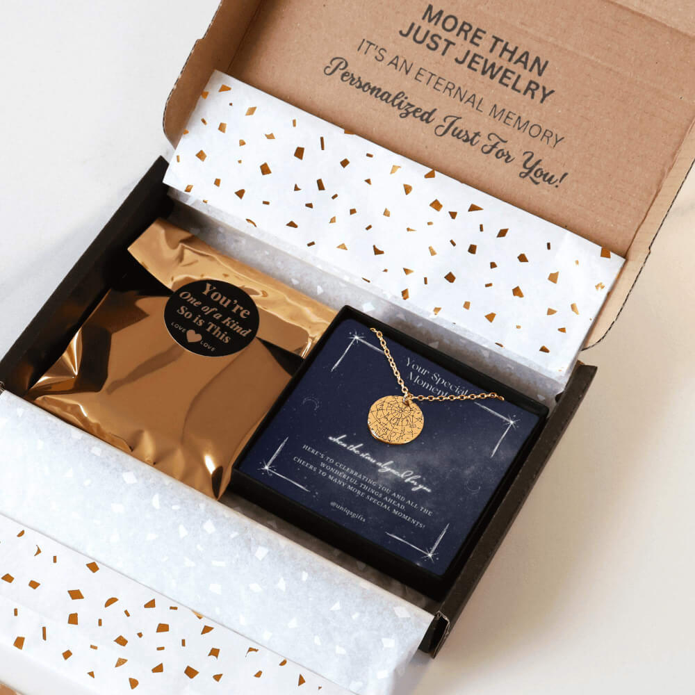 Personalized gold necklace with a coin pendant engraved in a custom star map, packaging in a gift box with a festive greeting card for any occasion, and gold confetti paper, held by hands against a neutral background.