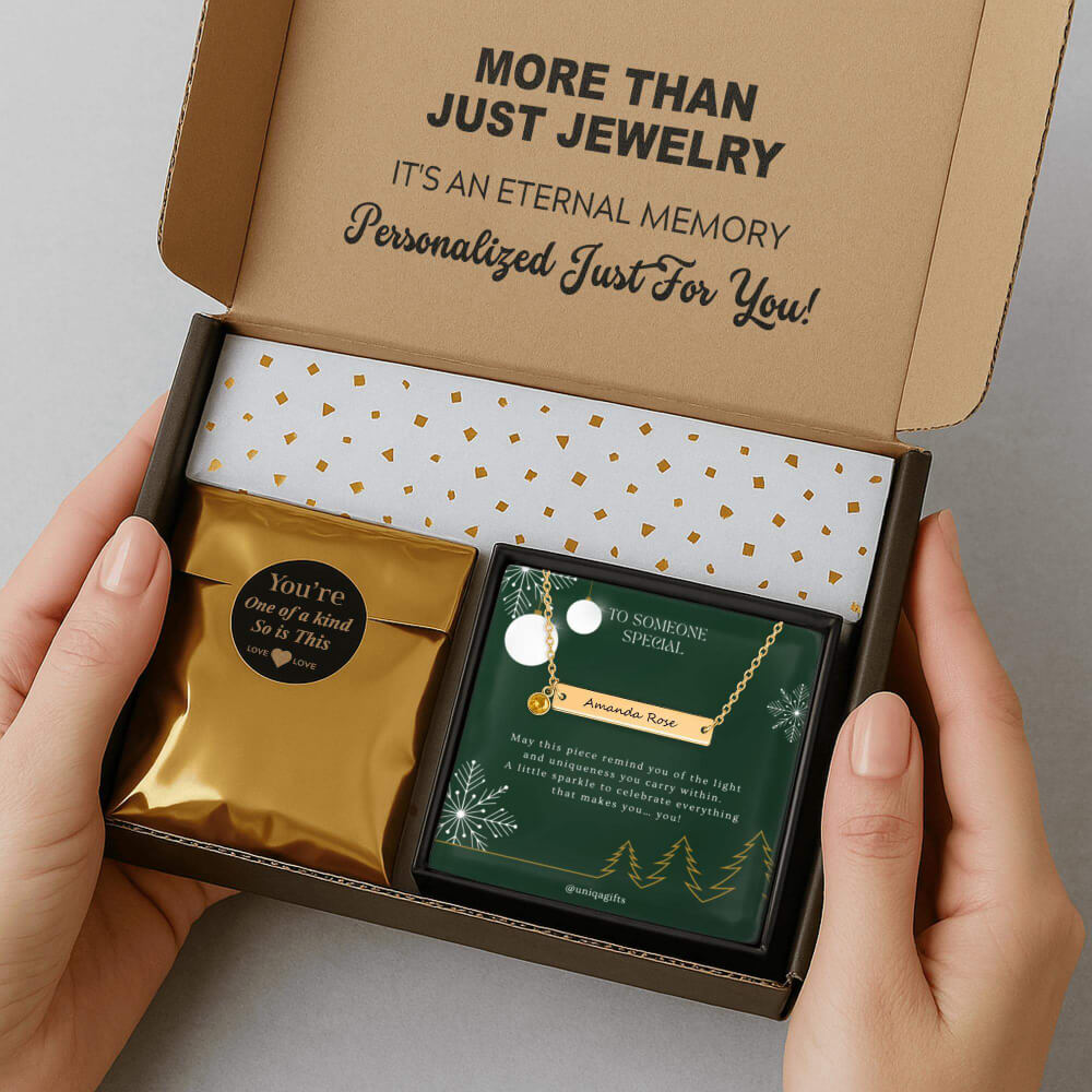 Personalized gold bar necklace with a birthstone, packaging in a gift box with a festive greeting card and gold confetti paper, held by hands against a neutral background.