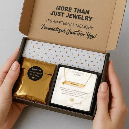 Personalized gold bar necklace with a birthstone, packaging in a gift box with a greeting card and gold confetti paper, held by hands against a neutral background.