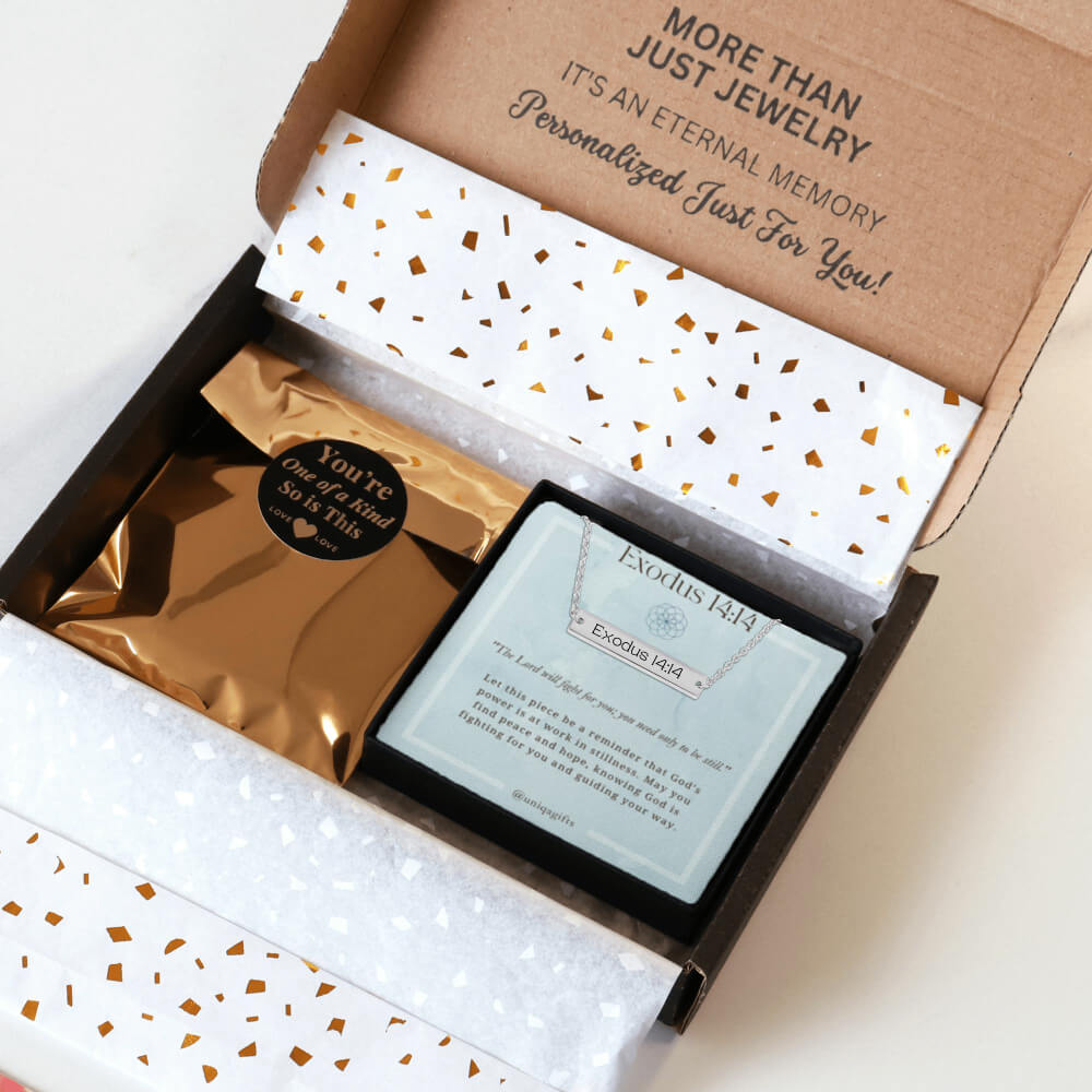 Personalized silver necklace with a bar pendant engraved with an inspirational bible verse, packaging in a gift box with a greeting card and gold confetti paper, held by hands against a neutral background.