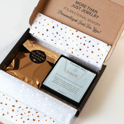 Personalized silver necklace with a bar pendant engraved with an inspirational bible verse, packaging in a gift box with a greeting card and gold confetti paper, held by hands against a neutral background.
