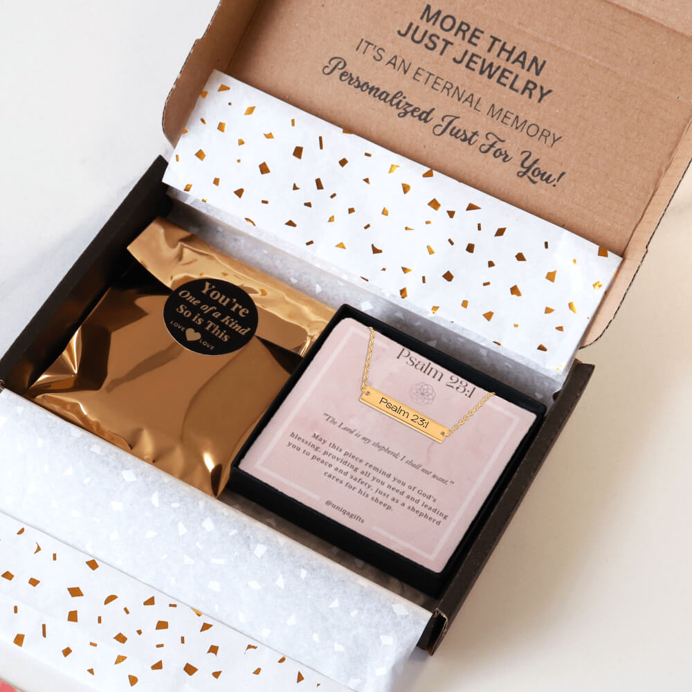 Personalized gold necklace with a bar pendant engraved with an inspirational bible verse, packaging in a gift box with a greeting card and gold confetti paper, held by hands against a neutral background.