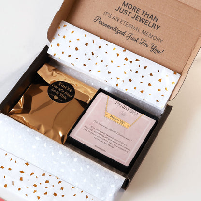Personalized gold necklace with a bar pendant engraved with an inspirational bible verse, packaging in a gift box with a greeting card and gold confetti paper, held by hands against a neutral background.