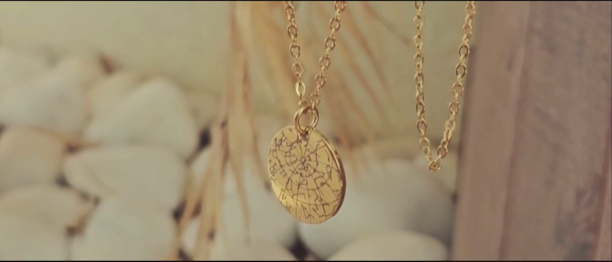 Load video: Rotating gold custom Star Map necklace showing the personalized back engraving, displayed on a light leaf background.