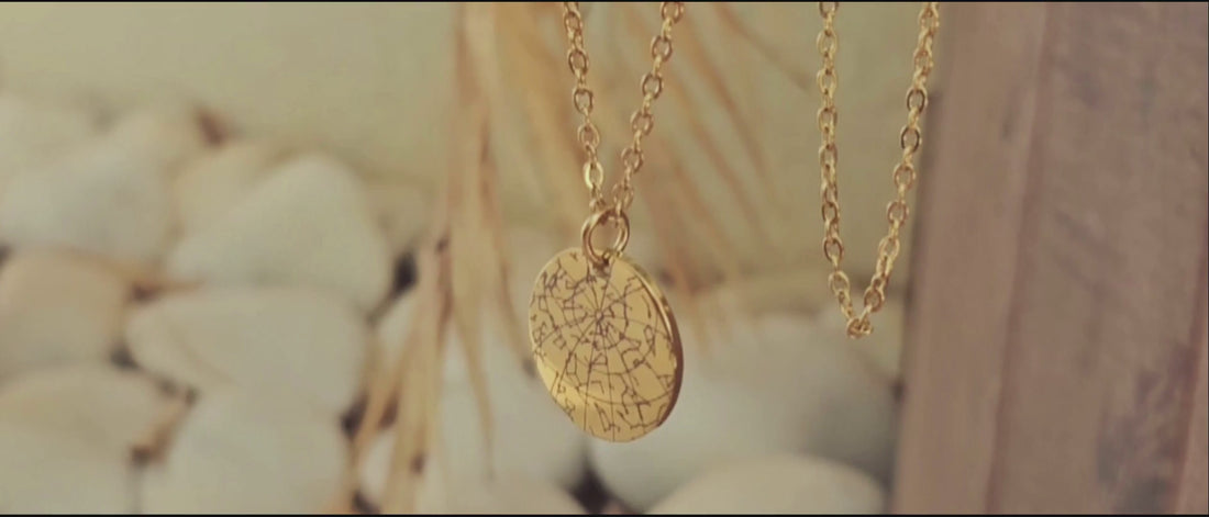 Rotating gold custom Star Map necklace showing the personalized back engraving, displayed on a light leaf background.