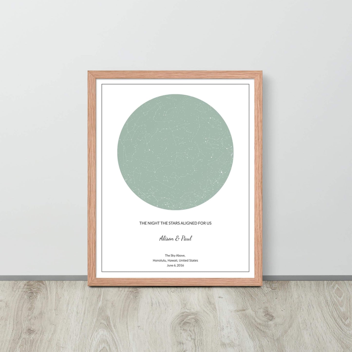 Sage green custom star map poster in a wood frame leaning against a light-colored wall on a light wood floor