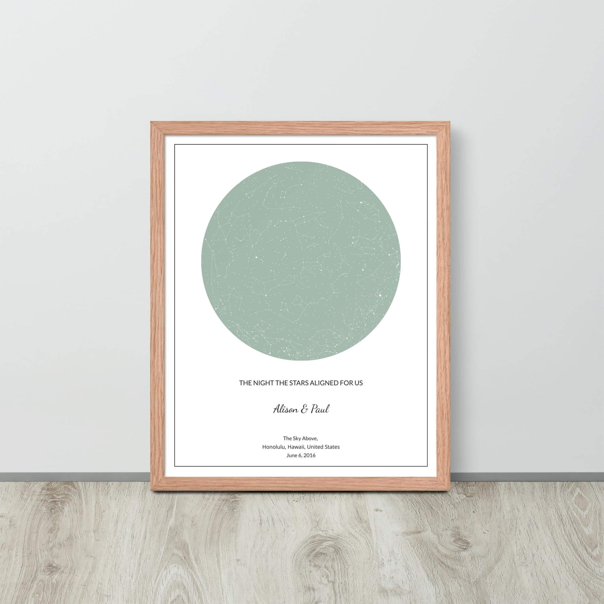 Sage green custom star map poster in a wood frame leaning against a light-colored wall on a light wood floor