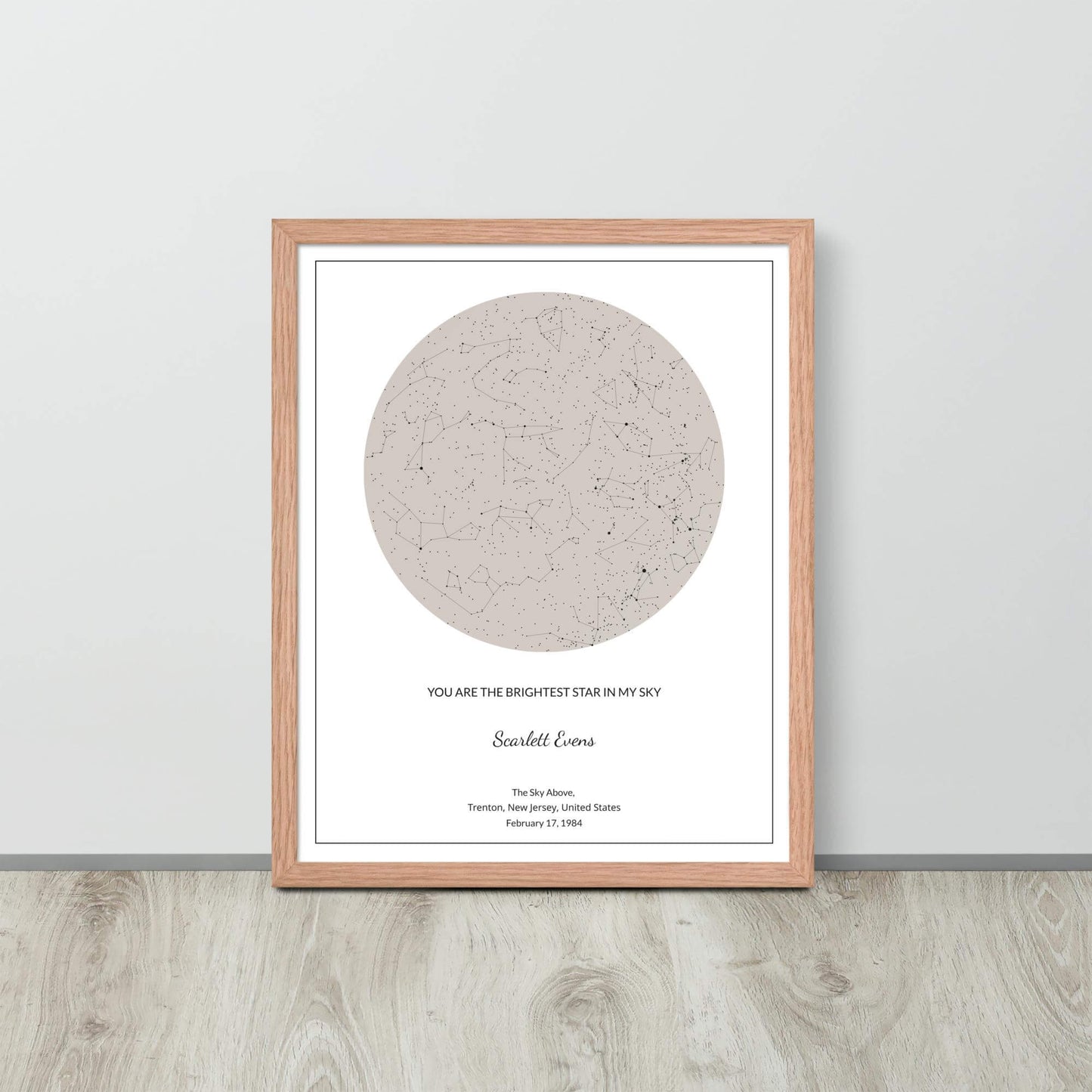 Soft Ambar custom star map poster in a wood frame leaning against a light-colored wall on a light wood floor.