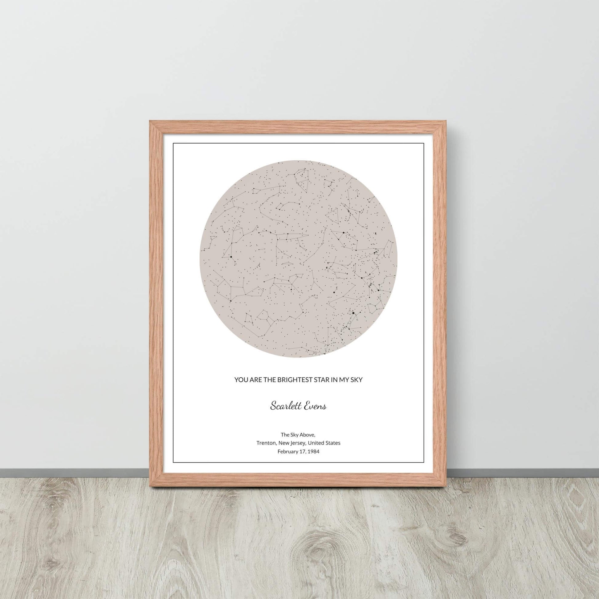 Soft Ambar custom star map poster in a wood frame leaning against a light-colored wall on a light wood floor.