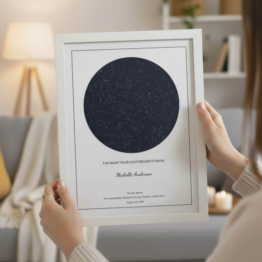 Framed star map poster in Midnight blue with a white frame with personalized text held by a woman in a warm home setting.