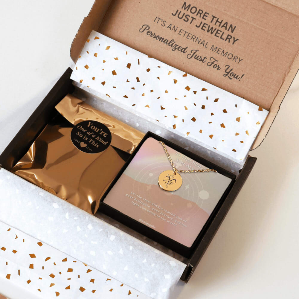 Personalized gold necklace with a coin pendant engraved in a zodiac sign and flower of the birth month, packaging in a gift box with a greeting card and gold confetti paper, held by hands against a neutral background.